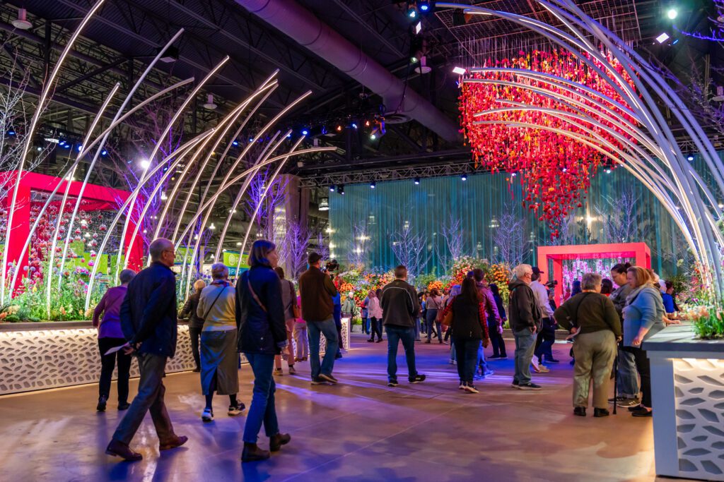 Groups of people walking under a display at the 2025 PHS Flower Show.