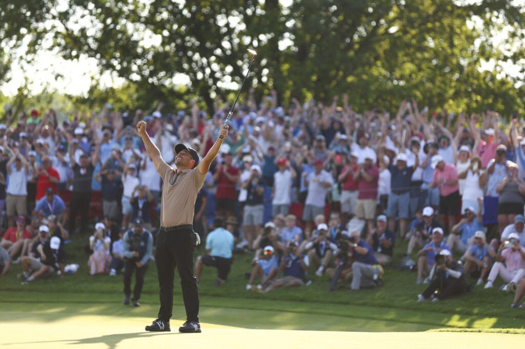 A golfer raises his arms in triumph on the field.