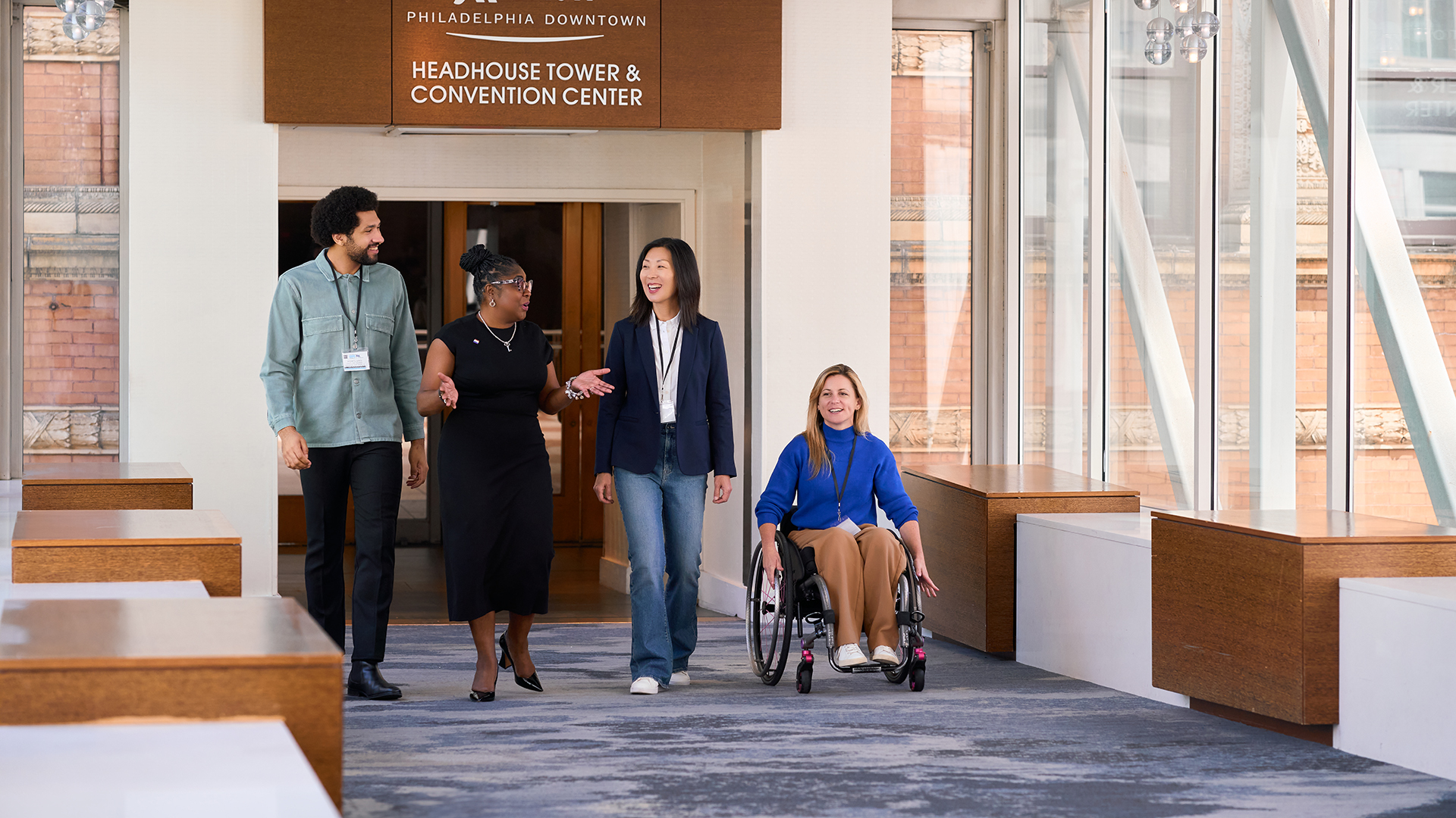 Four people cross the Marriott skywalk to the PA Convention Center. One person is in a wheelchair.