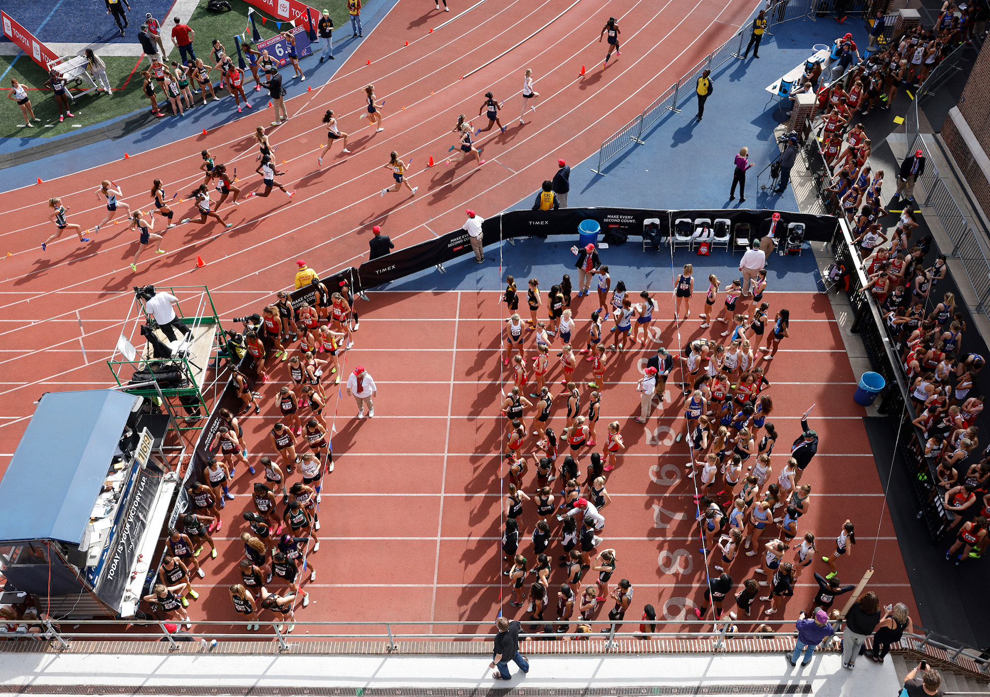 Overview shot of the Penn Relays. Several people are in a race while others line up for the next race.