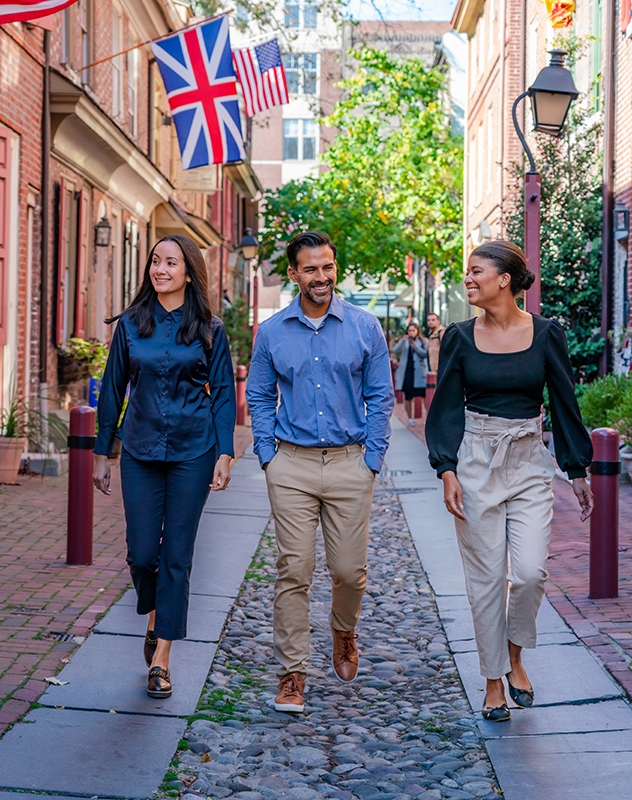 Three people dressed in business casual clothing walk down a historic cobblestone street in Philadelphia.