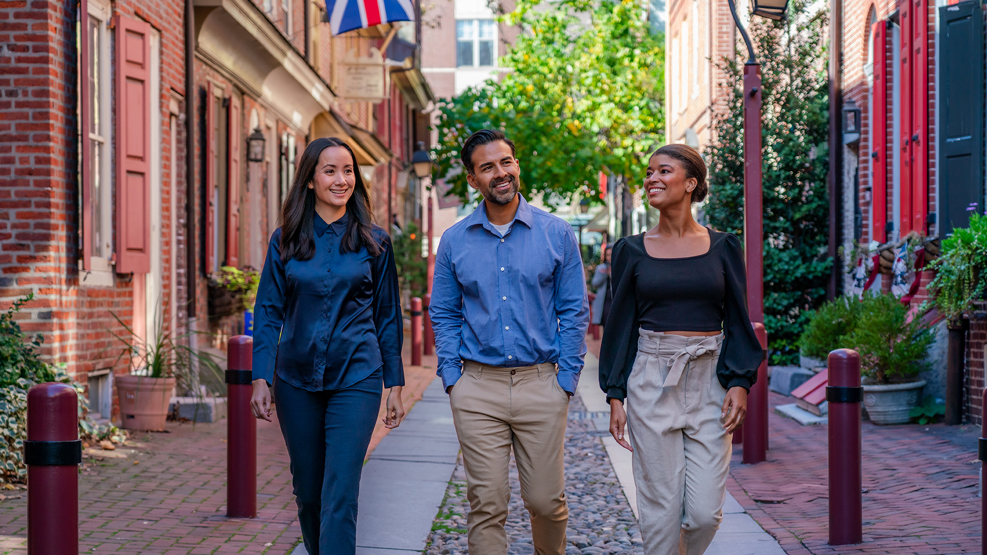 Three people dressed in business casual clothing walk down a historic cobblestone street in Philadelphia.