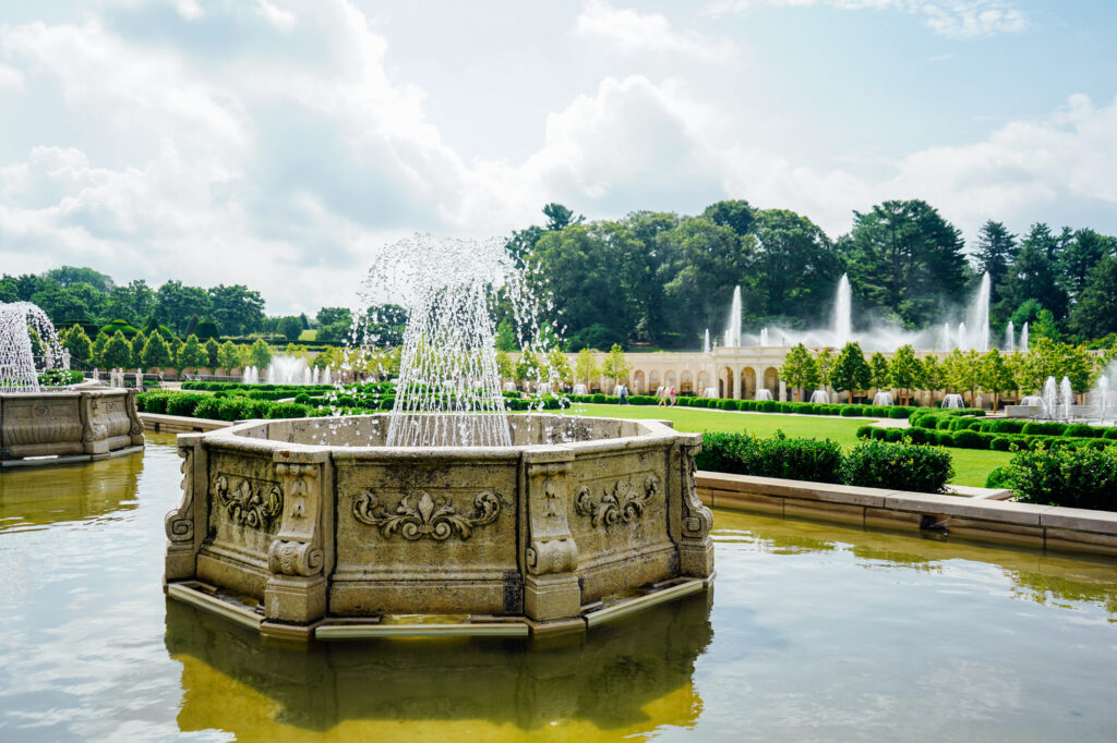 A fountain sits in the foreground with lush green hedges in the background