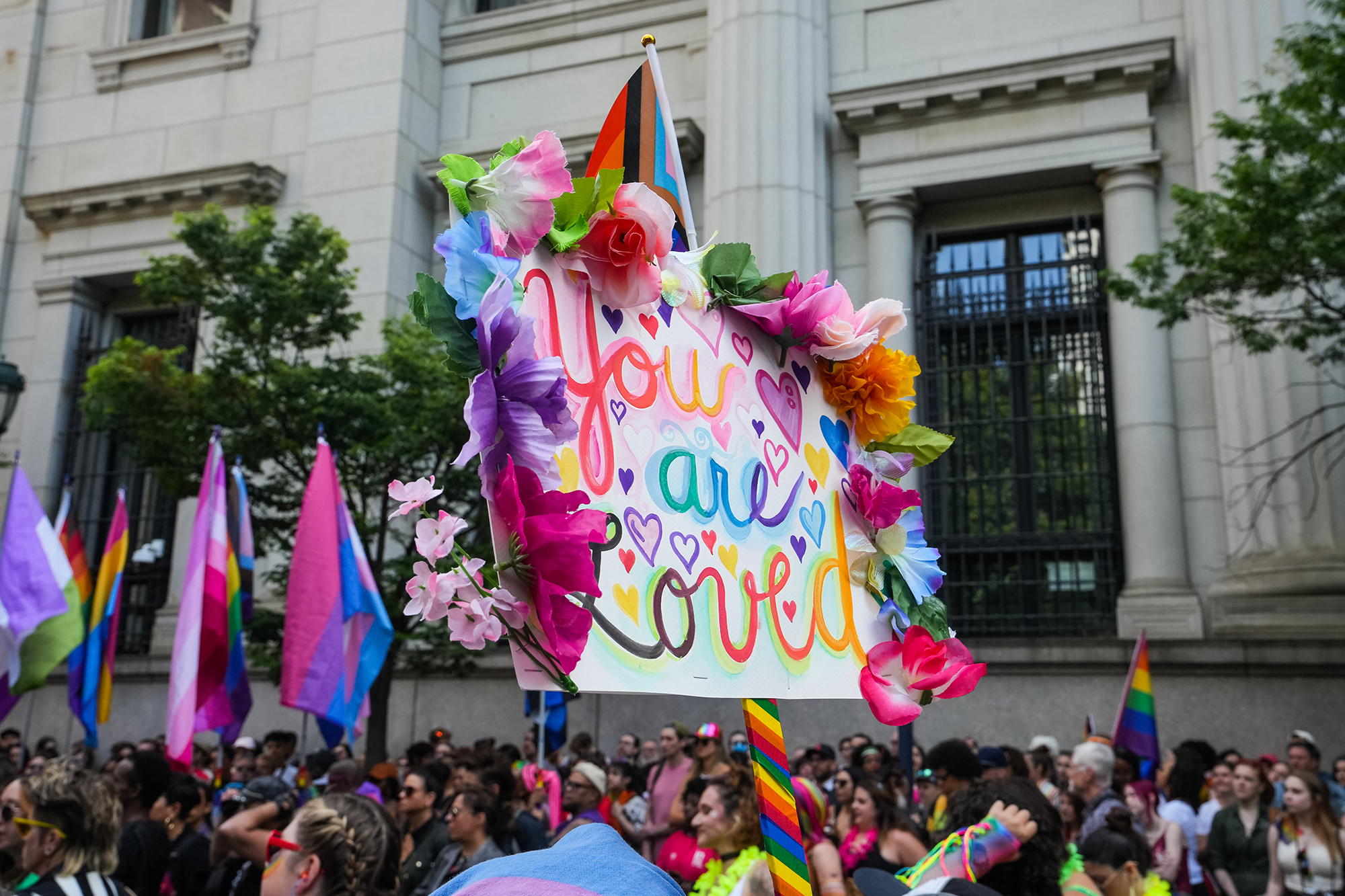 A parade of people during pride holding a sign that says "You are loved."