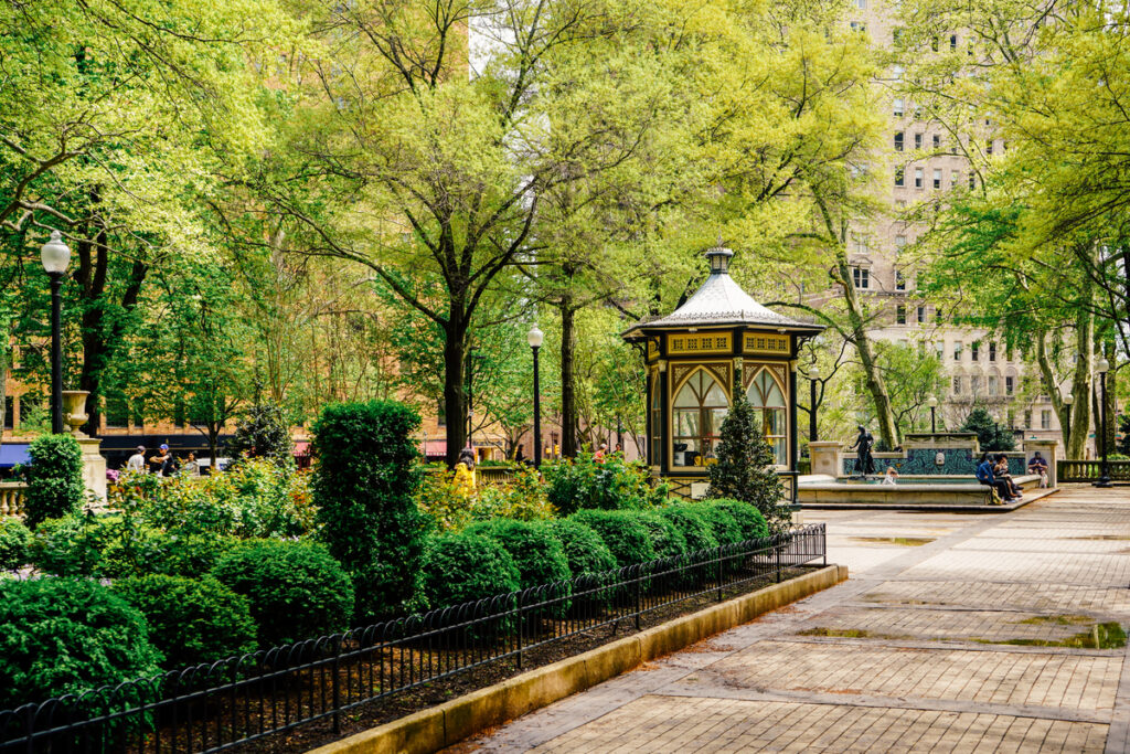 A lush, green park with a pergola in the center of a pedestrian walkway.