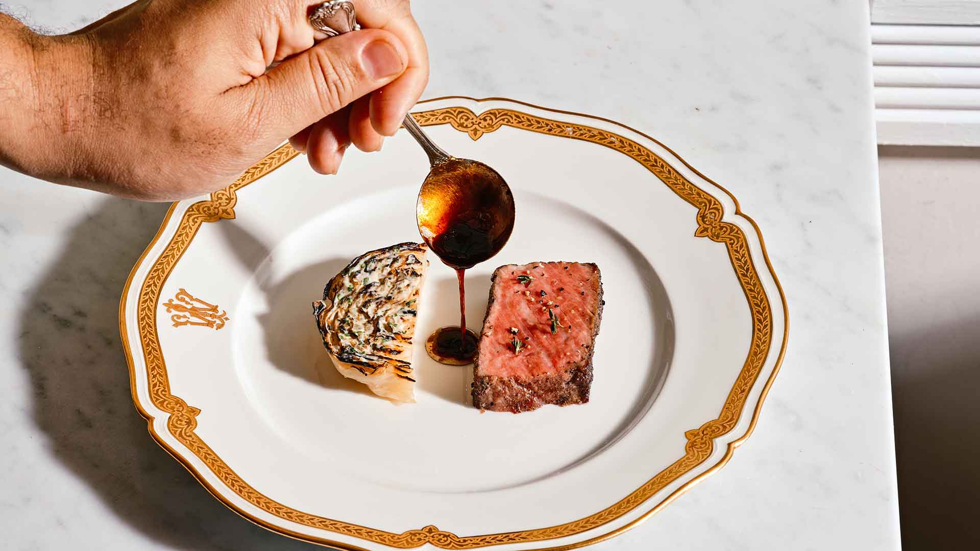 Someone adds sauce to a plate of steak and cabbage.