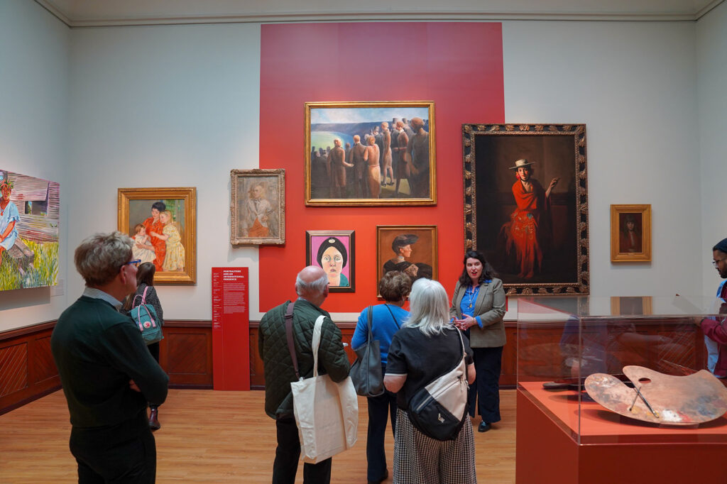 Museum visitors look at the paintings hung on the walls.