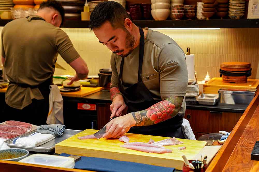 A chef carefully slices raw fish for sushi.
