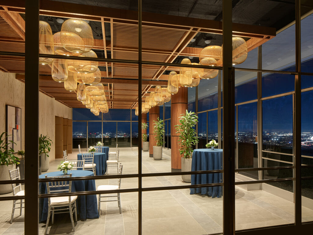 A rooftop events space with large glass walls and high tops tables looking over the city skyline.