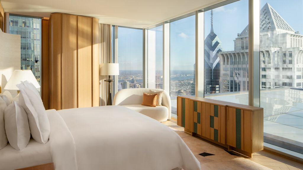 A hotel room with huge windows looks out onto the Philadelphia skyline.