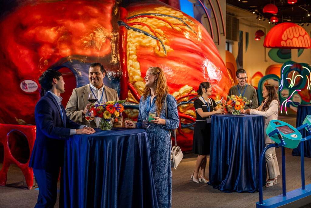 Several people network at high tops in front of the Franklin Institute's Giant Heart.