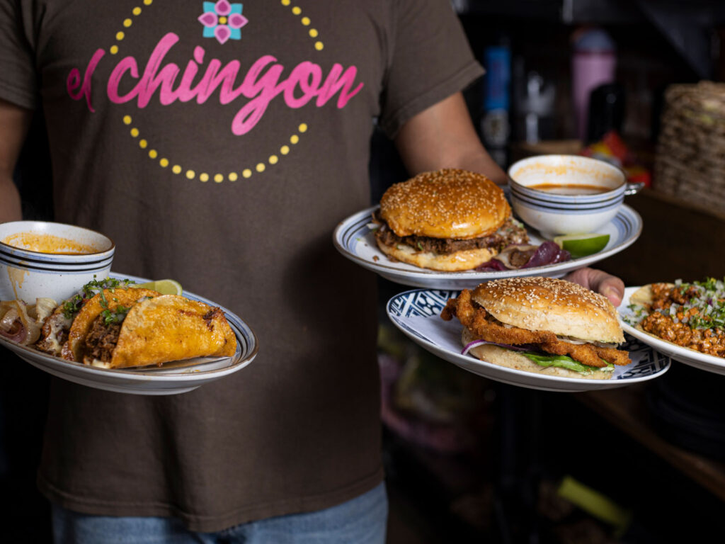 A waiter holds many plates of food including burgers and sandwiches