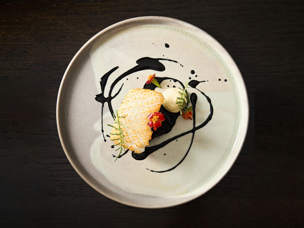 A plate of fine dining food on a dark table.