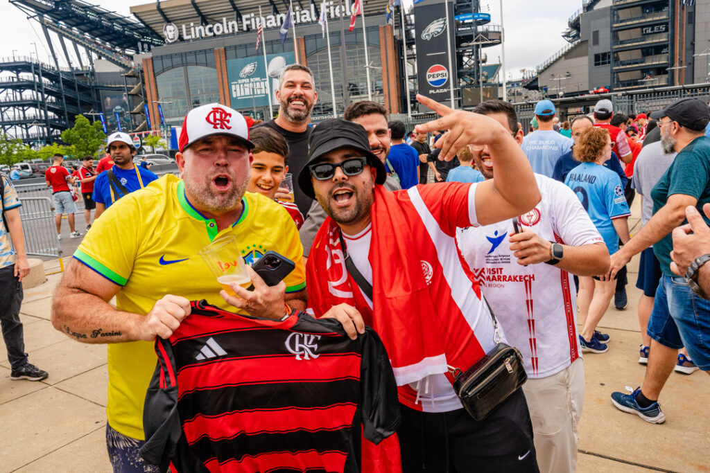 Fans of the Clob World Cup stand outside of the stadium holding up jerseys for their teams.