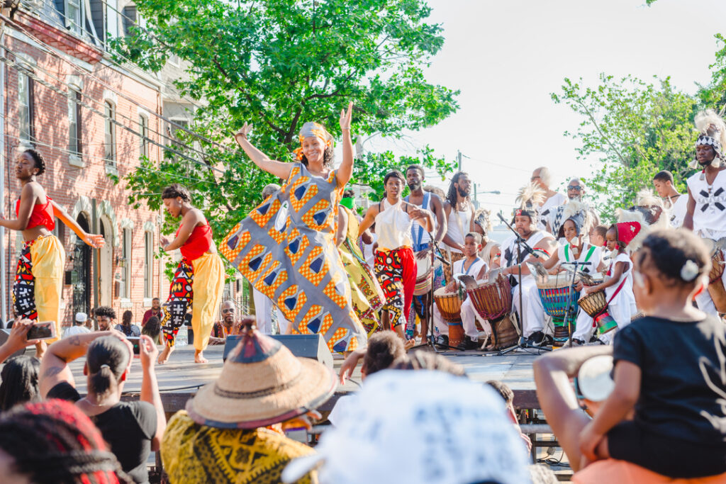 A woman stands on stage and claps along to music in front of a large crowd.