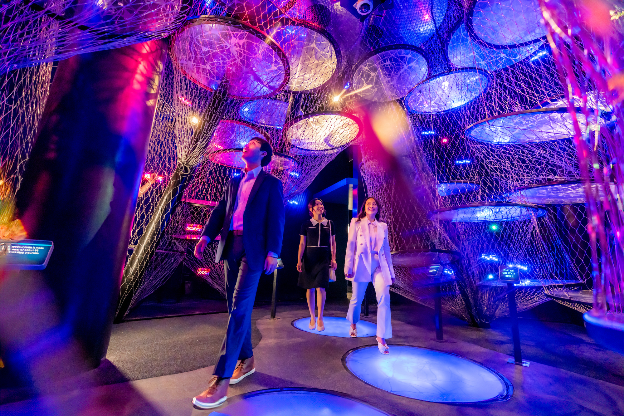 Three people walk through a colorful exhibit with nets.