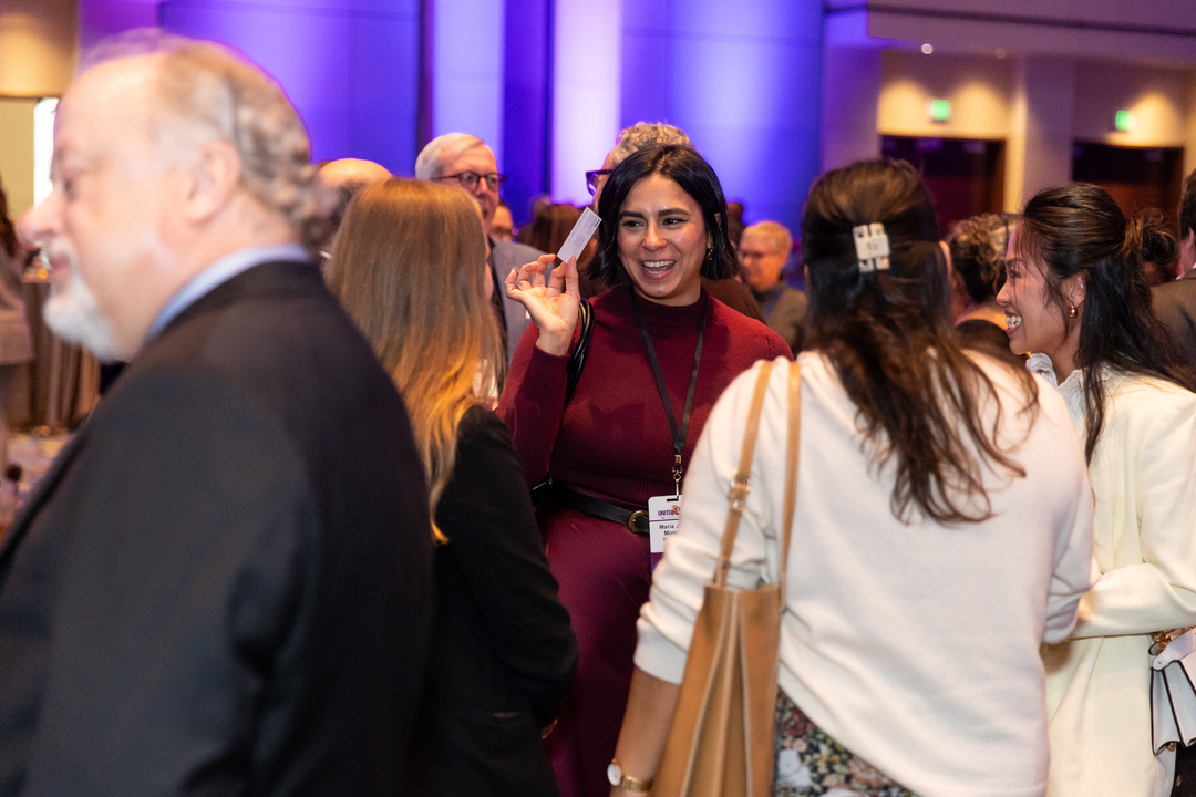 A group of people talk and laugh during na event, one person holds up a business card.