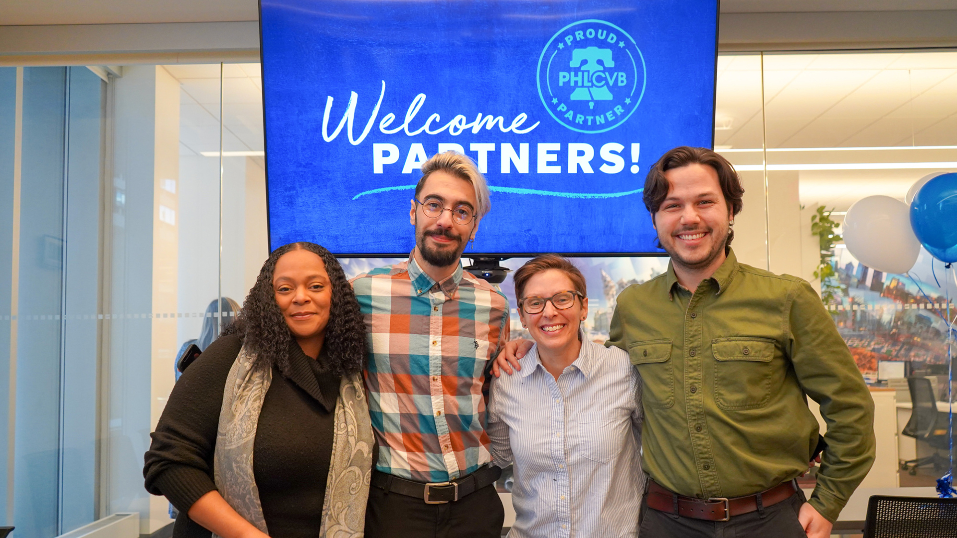 Four people pose for a photo in front of a a screen that says 
