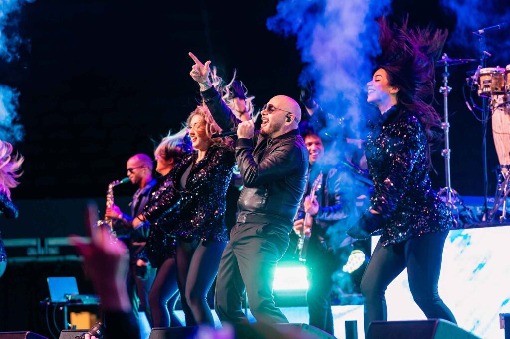 Pitbull on stage singing, surrounded by backup dancers.