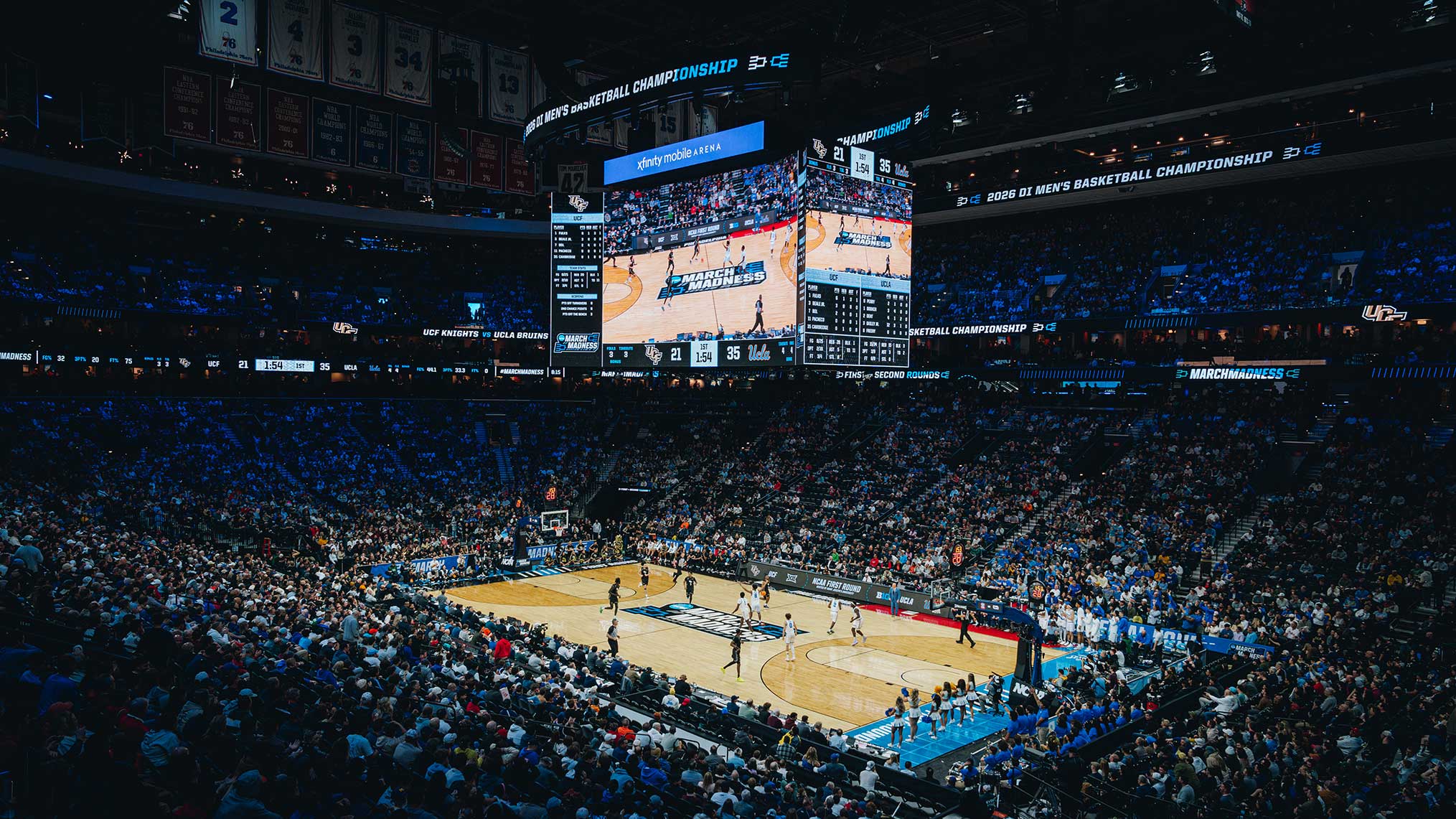 In the center of a full stadium is a March Madness basketball game.