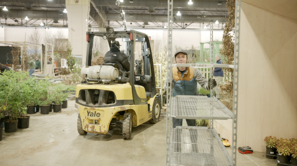 A man pushes a cart through the Convention Center showrrom while a man drives a forklift behind him.