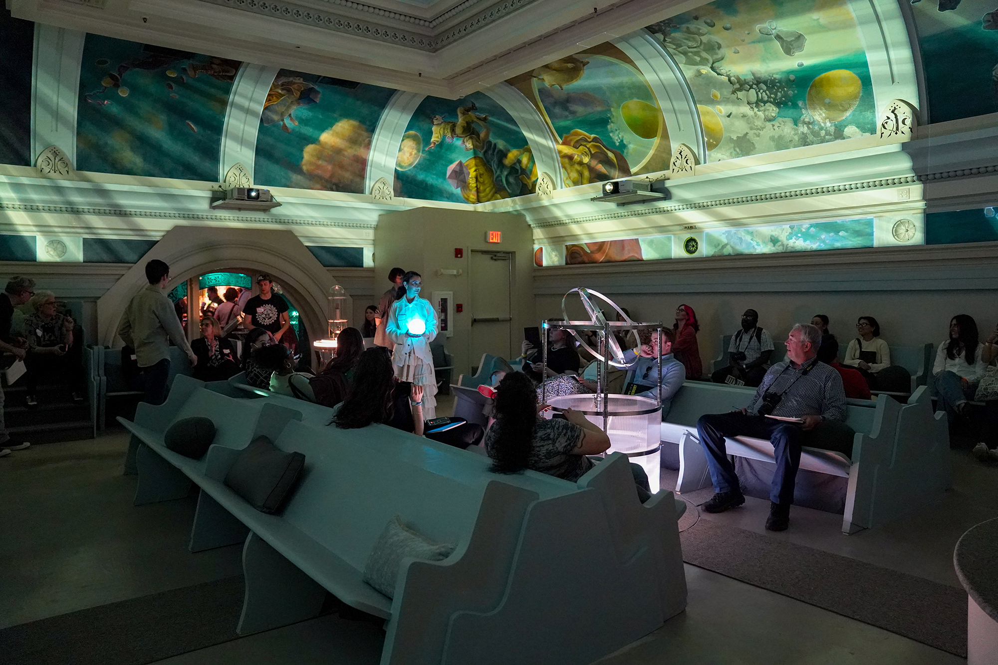 Ina. dark room a group of people look at an art projection on the ceiling.
