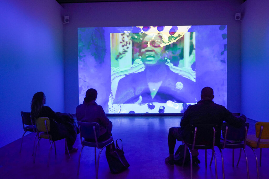 A group of people watch a video installation at the Freedom Dreams gallery.