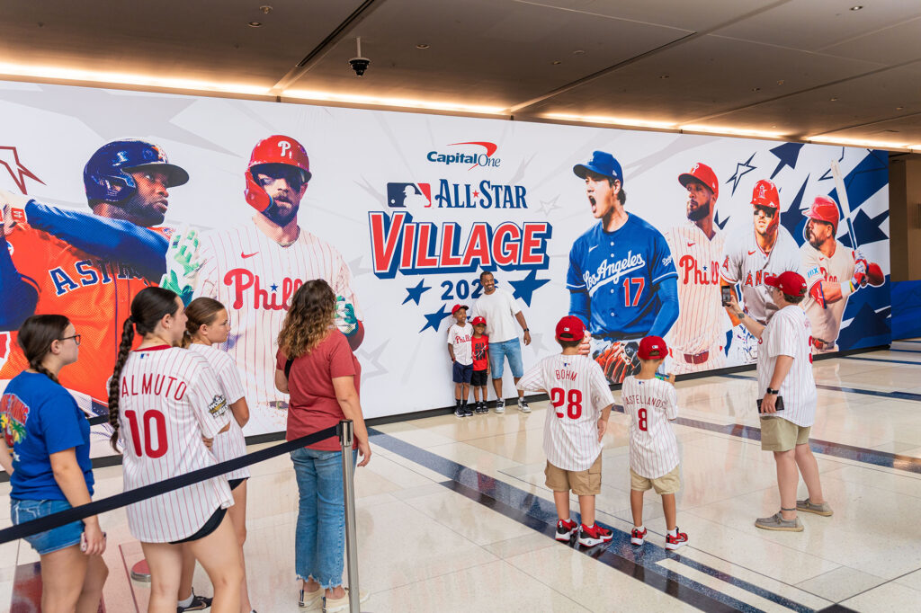 A family poses for a photo in front of the MLB All-Star Village backdrop.