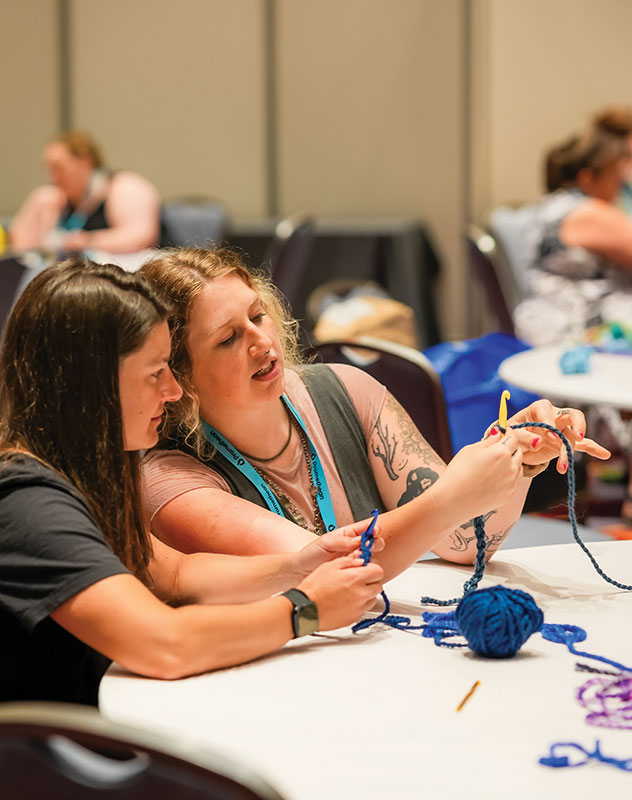 Two people practice knitting in a meeting space in the PA Convention Center