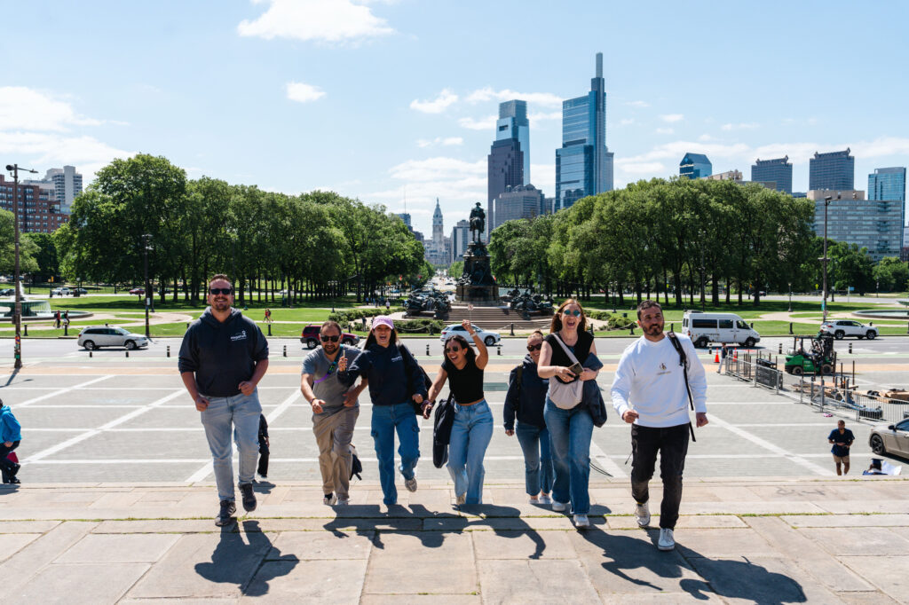 A group of tourists run up the Rocky Steps in Philadelphia with the city skyline in the background.